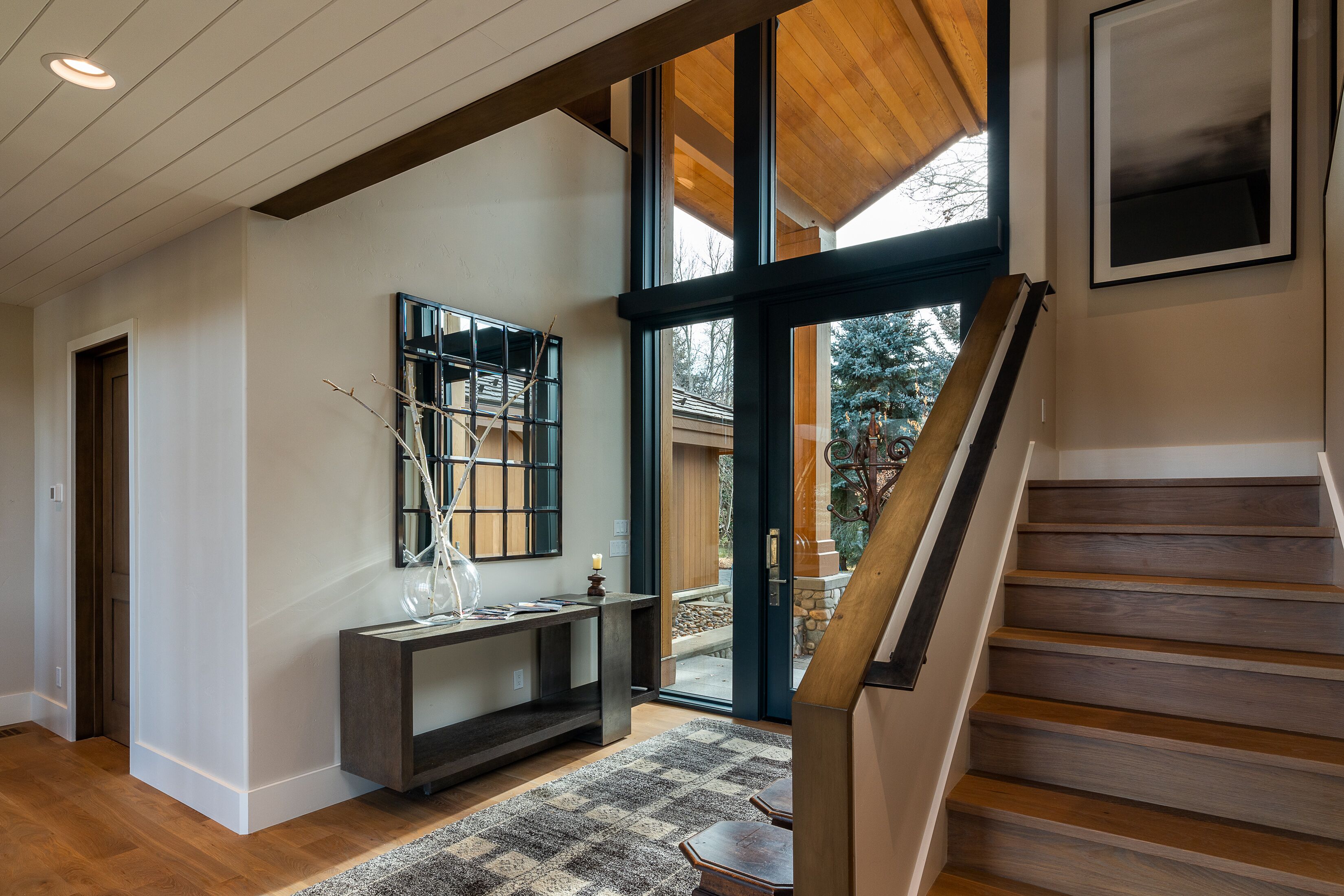Un intérieur moderne avec un escalier en bois, une grande fenêtre et une console agrémentée d’objets décoratifs.