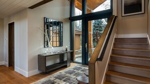 A modern interior with a wooden staircase, a large window, and a console table with decorative items. - Luxurious Sun Valley Mountain Retreat on Golf Course (Sun Valley)