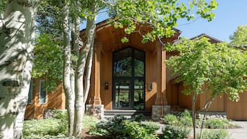 Une maison en bois avec une grande porte d’entrée, des marches en pierre et un jardin où poussent différentes espèces de plantes.