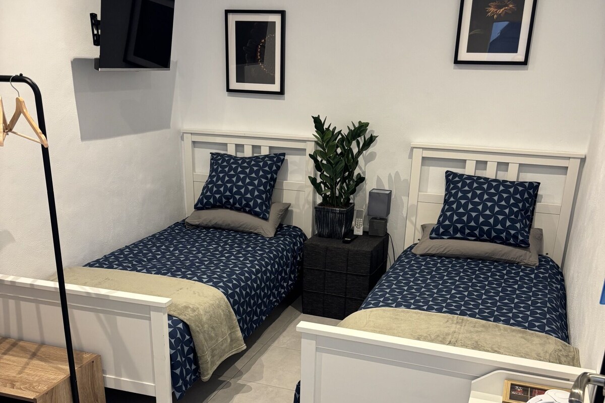 Une chambre d’hôtel avec deux lits, un bureau, une chaise, une télévision et une poubelle.