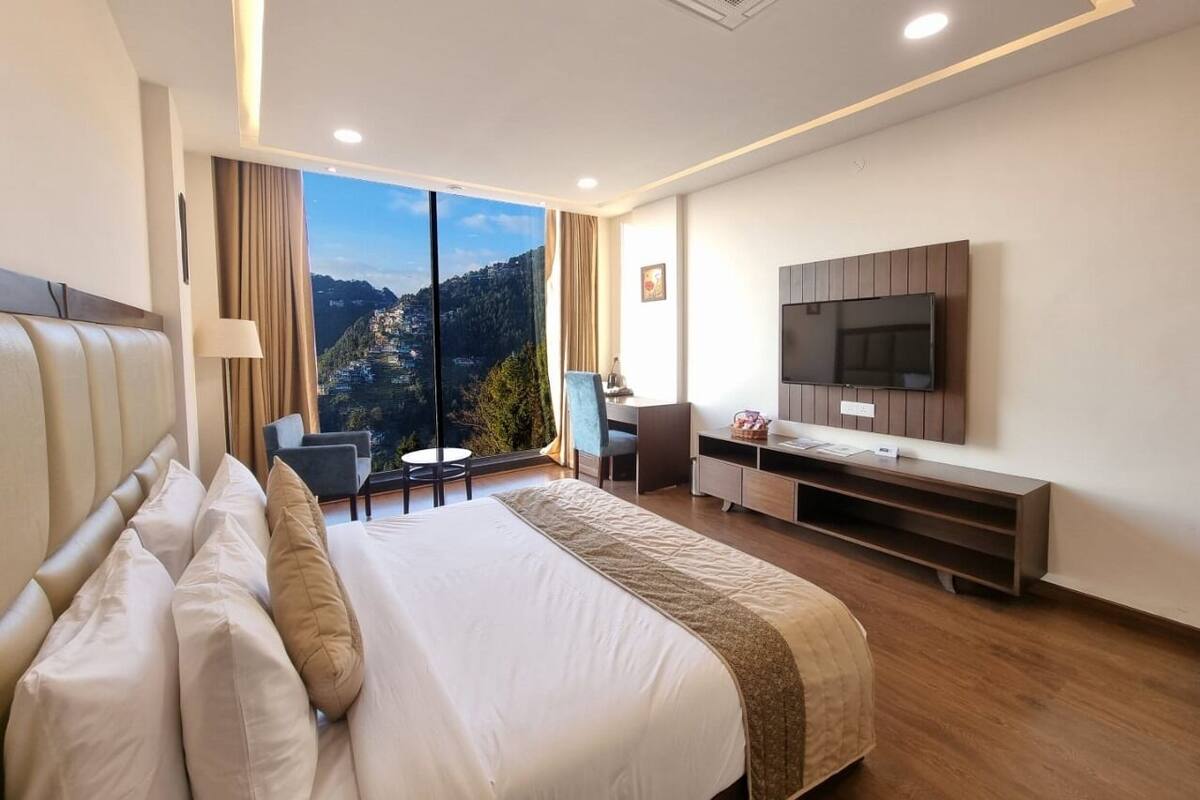 Une chambre d’hôtel avec un grand lit, un bureau, une chaise, une télévision et une vue sur un paysage montagneux.