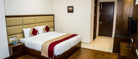 A hotel room with a large bed, wooden flooring, a TV, and a door leading to another room.
