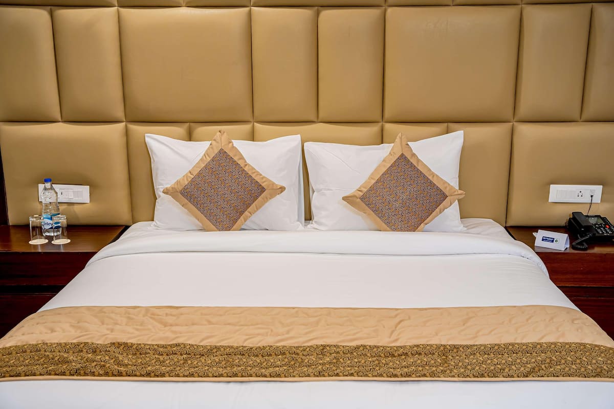 Une chambre d’hôtel avec un grand lit, deux coussins décoratifs, une table de chevet avec une bouteille d’eau, un téléphone et une prise électrique.