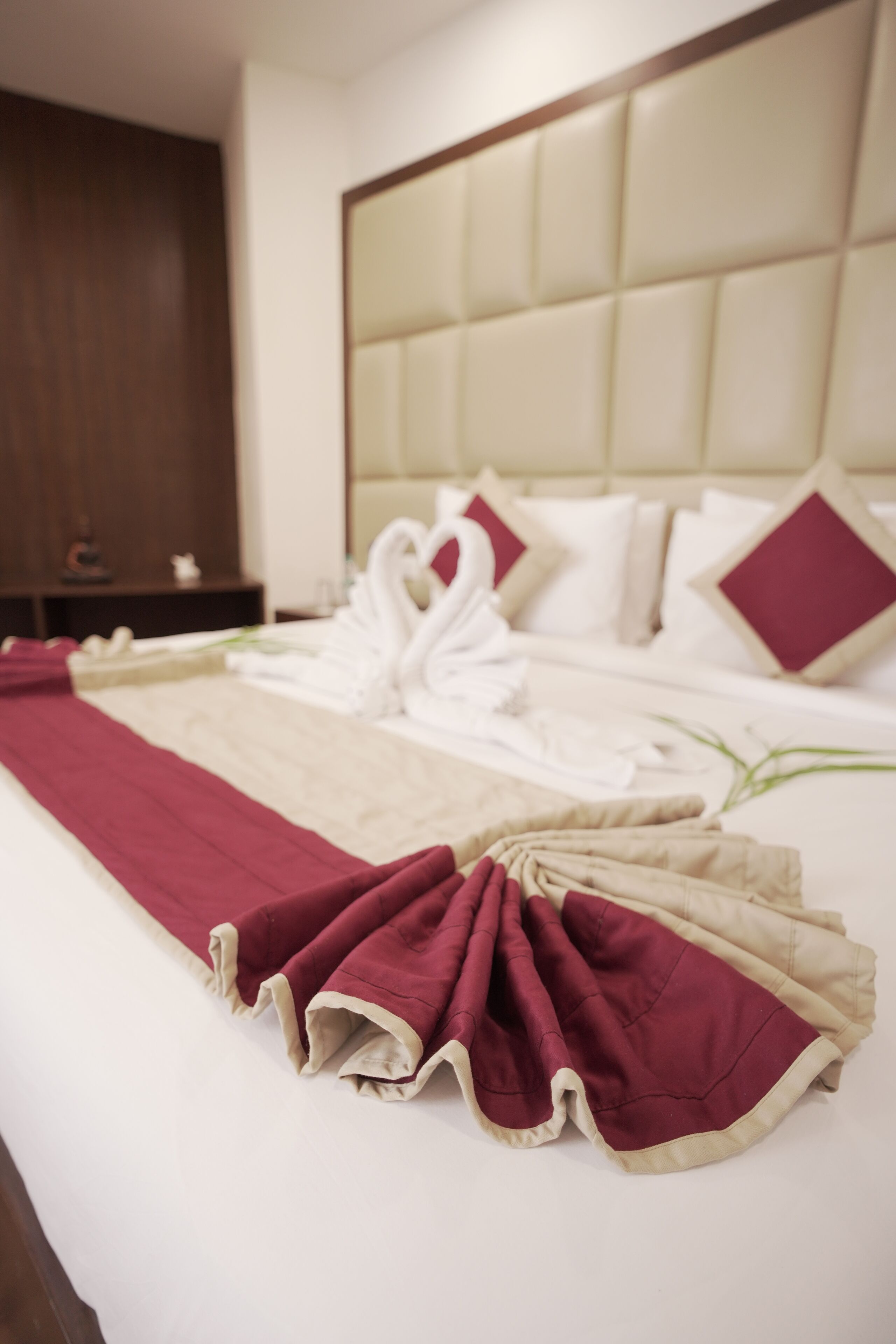 A neatly made bed with a red and beige bedspread, white pillows, and a decorative swan headpiece.