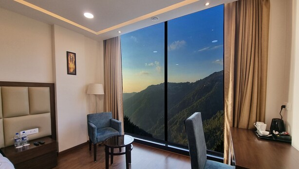 Una habitación de hotel con un ventanal grande, una cama, un escritorio con lámpara y una silla.