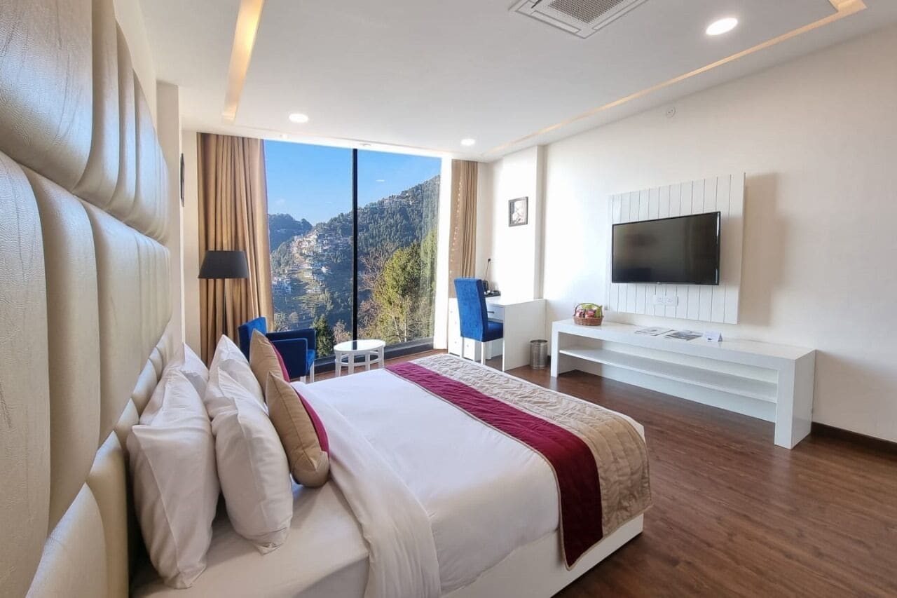 A modern hotel room with a large bed, a TV mounted on the wall, a desk, and a chair.