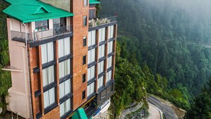 Un edificio de varios pisos con techo verde, situado en una ladera con vista a un valle boscoso.