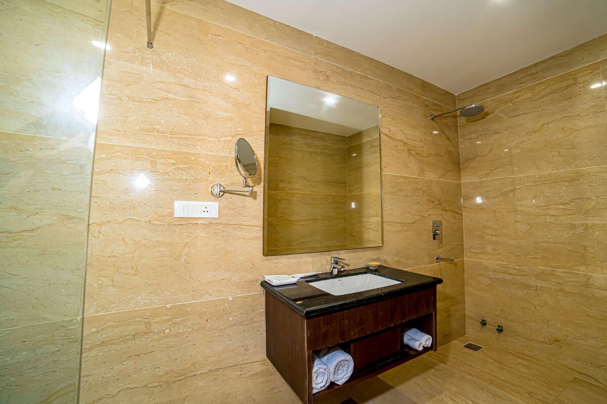 Uma casa de banho com parede de mármore, lavatório com espelho e chuveiro.