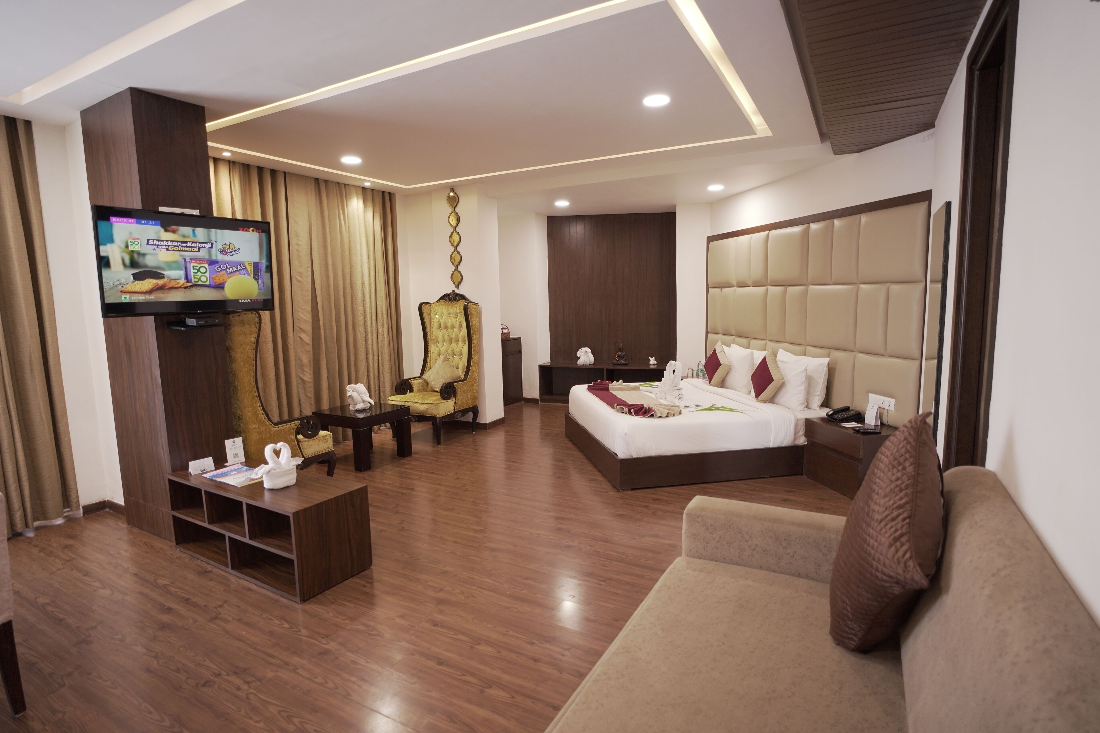 A modern hotel room with a large bed, a sofa, a TV, and a seating area with a chair and a small table.