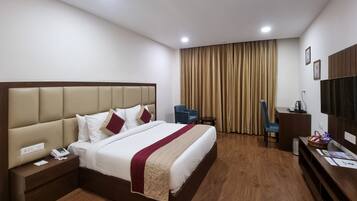 Habitación de hotel con una cama grande, un escritorio, una silla, un televisor y una ventana con cortinas.