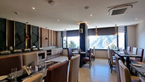 Un comedor moderno con mesas y sillas altas, una barra de cocina y grandes ventanales con vistas al exterior.