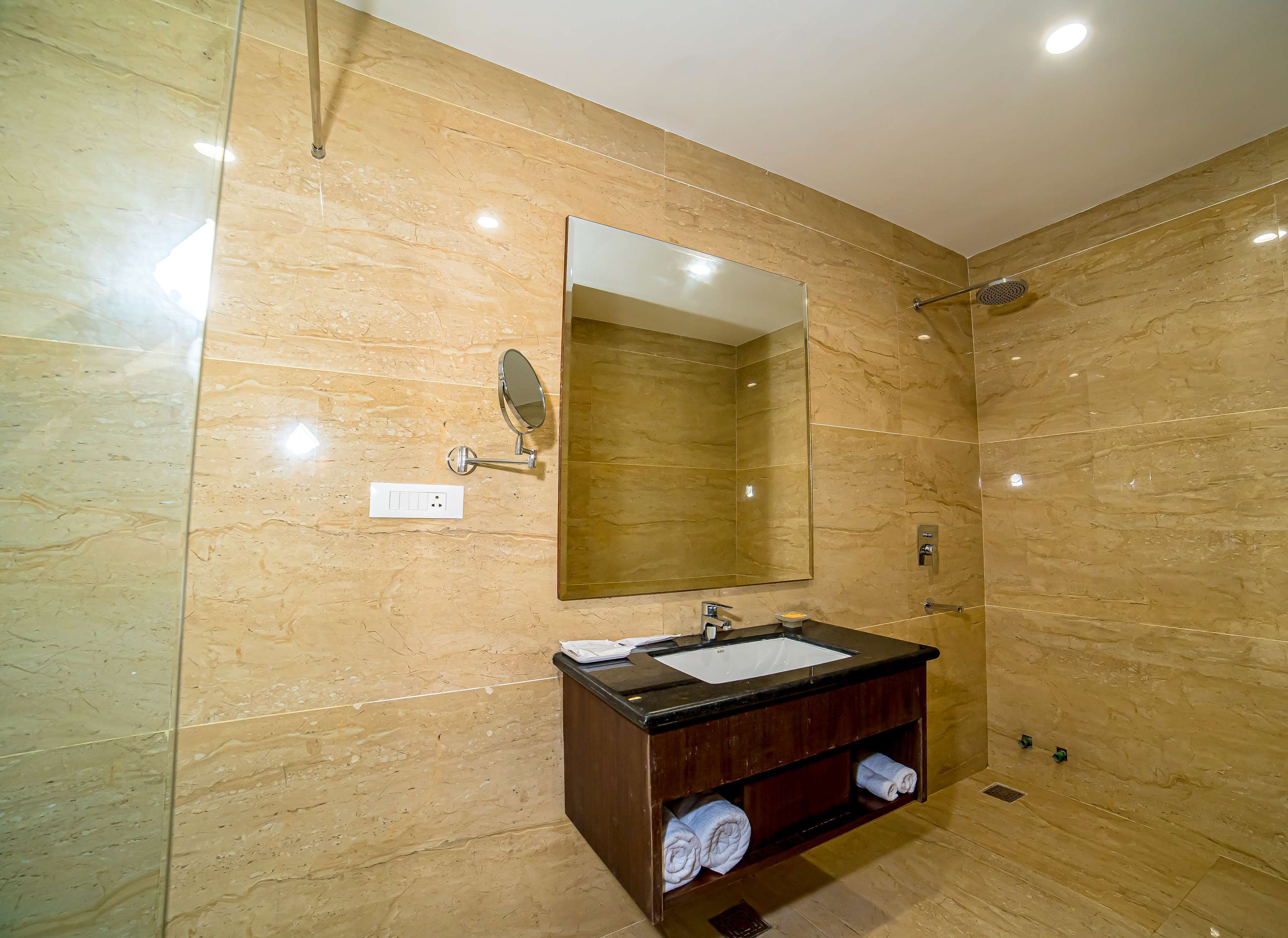A bathroom with a marble wall, a large mirror, a sink with a wooden vanity, and a shower area.