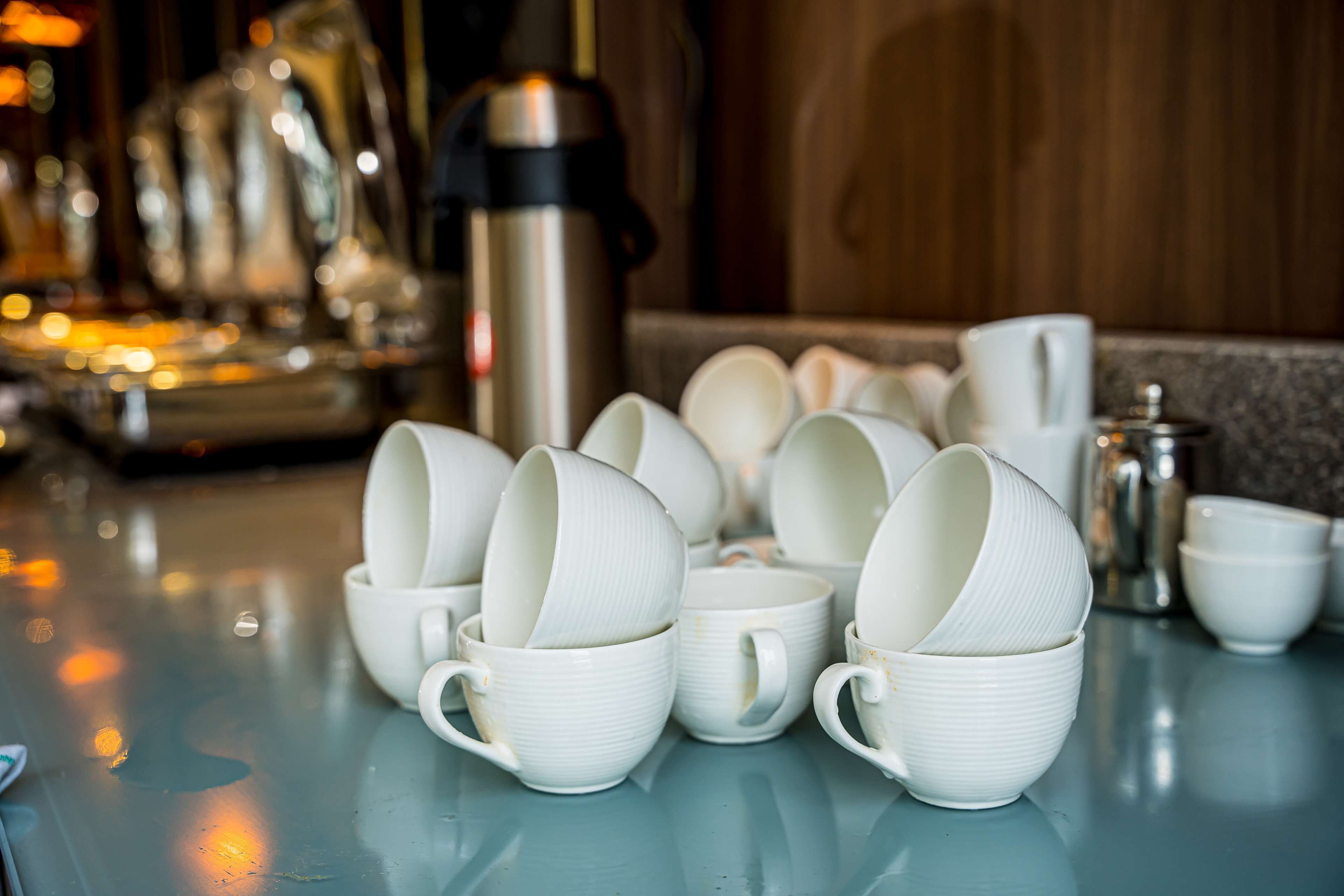Una mesa con varias tazas de cerámica blanca y un termo de acero inoxidable.