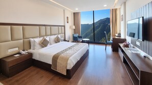 Habitación de hotel con una cama grande, televisión, escritorio y vista a un paisaje montañoso.