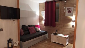 Una habitación acogedora con un sofá, una mesita con una botella y vasos, un televisor montado en la pared y un panel de pared de madera.