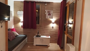 Una habitación acogedora con pared de madera, una cama con almohadones estampados, una mesita de noche con una botella y vasos, y una decoración con forma de corazón.