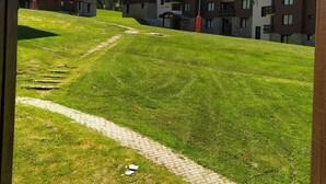 Un área verde con un sendero pavimentado que conduce a un conjunto de edificios con varios balcones y una montaña al fondo.