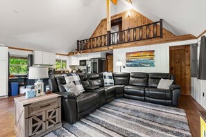 A spacious living area with a large black leather sectional sofa, a wooden dining table, and a kitchen in the background. - Lakefront Home-Stunning Views-Hot Tub, 3100 sqft! (Wakefield)