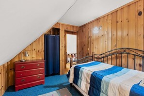 A bedroom with a sloped ceiling, a bed with a blue and beige quilt, a red dresser, and a wooden wall. - Lakefront Home-Stunning Views-Hot Tub, 3100 sqft! (Wakefield)