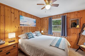 A bedroom with a bed, a nightstand, a lamp, a painting, a window with curtains, and a ceiling fan. - Lakefront Home-Stunning Views-Hot Tub, 3100 sqft! (Wakefield)