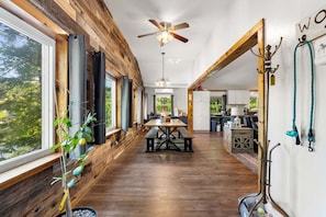 A spacious kitchen with wooden beams, a dining area with a table and benches, and a view of the outdoors through large windows.