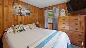 A wooden-paneled room with a bed, a dresser, a painting, and a sign indicating a guest room. - Lakefront Home-Stunning Views-Hot Tub, 3100 sqft! (Wakefield)
