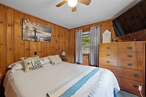 A wooden-paneled room with a bed, a dresser, a painting, and a sign indicating a guest room. - Lakefront Home-Stunning Views-Hot Tub, 3100 sqft! (Wakefield)