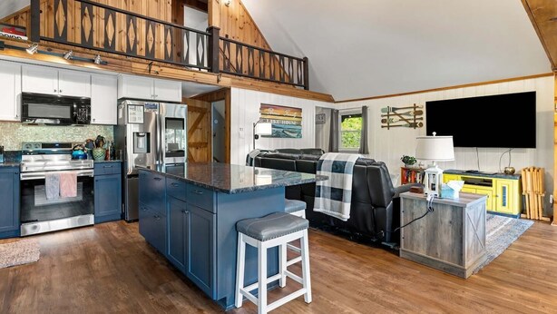 A spacious kitchen with modern appliances, a dining area with a high ceiling and wooden beams, and a flat-screen TV mounted on the wall. - Lakefront Home-Stunning Views-Hot Tub, 3100 sqft! (Wakefield)