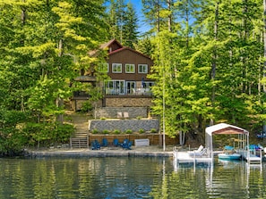 A lakeside cabin with a deck, a dock with boats, and a stone retaining wall.