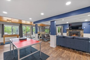 A modern living room with a ping pong table, a fireplace, and a comfortable seating area. - Lakefront Home-Stunning Views-Hot Tub, 3100 sqft! (Wakefield)