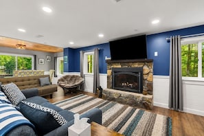 A living room with a stone fireplace, a sofa, a chair, and a television. - Lakefront Home-Stunning Views-Hot Tub, 3100 sqft! (Wakefield)