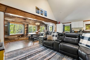A spacious living area with a large black leather sofa, a wooden accent wall, and a dining table with chairs. - Lakefront Home-Stunning Views-Hot Tub, 3100 sqft! (Wakefield)