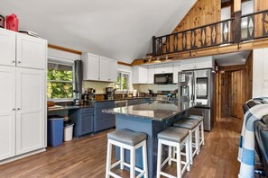 A modern kitchen with a central island, bar stools, and a wooden upper level.