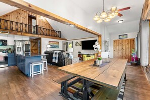 Una amplia cocina estilo loft con techo de madera, un comedor con una gran mesa de madera y un televisor montado en la pared.