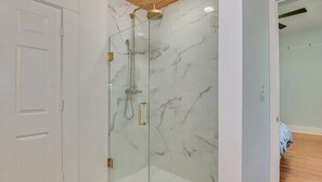 A glass-enclosed shower with a marble wall, a white door, and a wooden ceiling. - Cute and Convenient Summerville Cottage (Augusta)