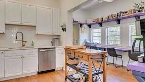 A modern kitchen with white cabinets, a wooden table, and a bookshelf.