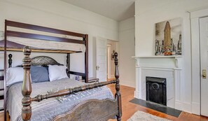 A bedroom with a four-poster bed, a fireplace, and a painting of a cityscape. - Cute and Convenient Summerville Cottage (Augusta)