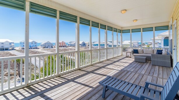 A covered porch with a view of beach houses, a wooden deck, and a seating area with a bench and a sofa.