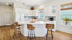 A modern kitchen with white cabinetry, a central island with bar stools, a microwave, stove, and a coffee maker.