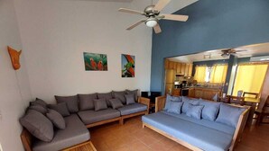 A living room with a sofa set, a wooden bench, and a ceiling fan. - 2 Bed 2 Bath condo with pool, full kitchen, in the marine sunset condos. (Playa del coco)