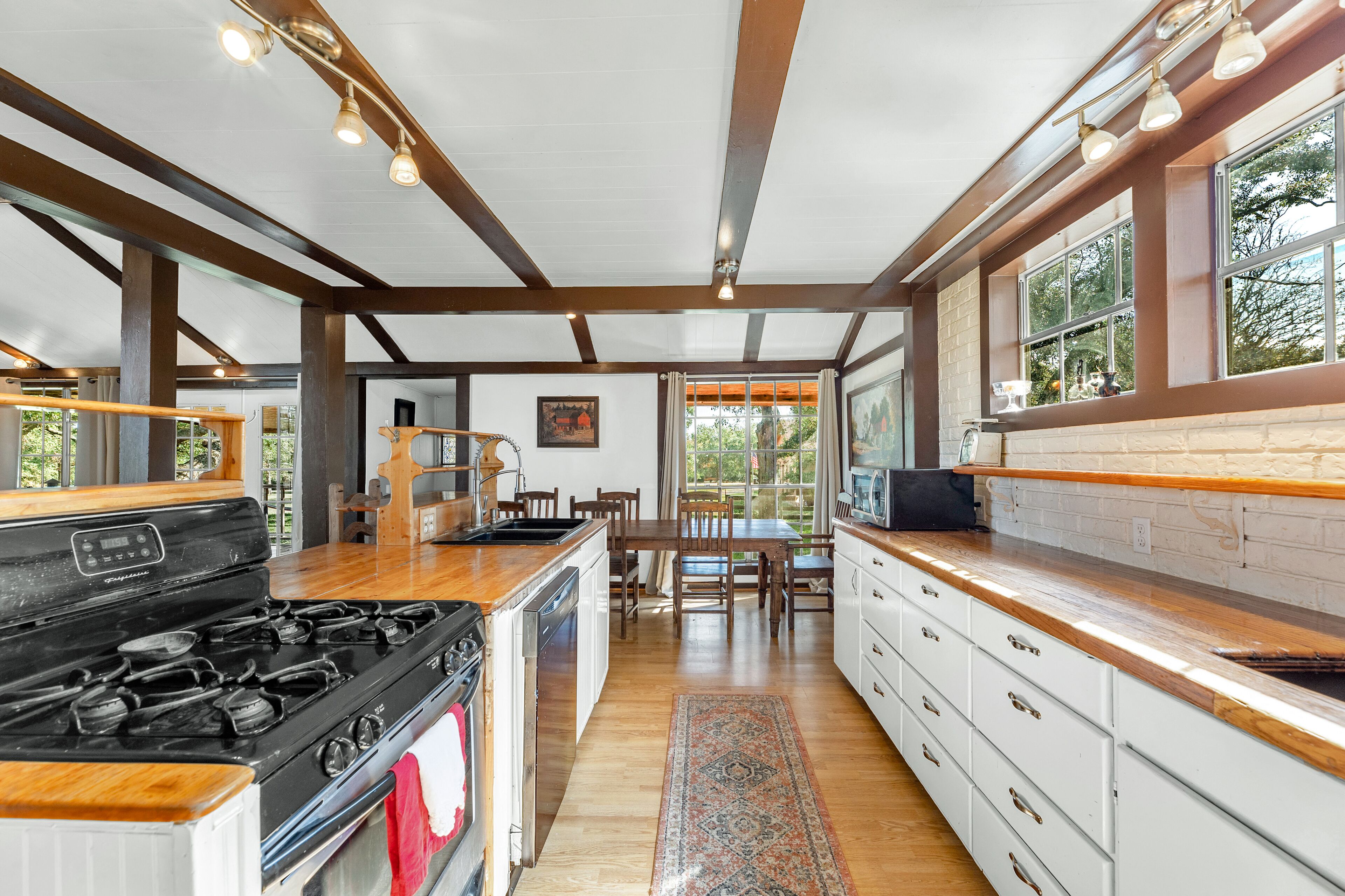 A modern kitchen with a central island, wooden beams, and large windows.