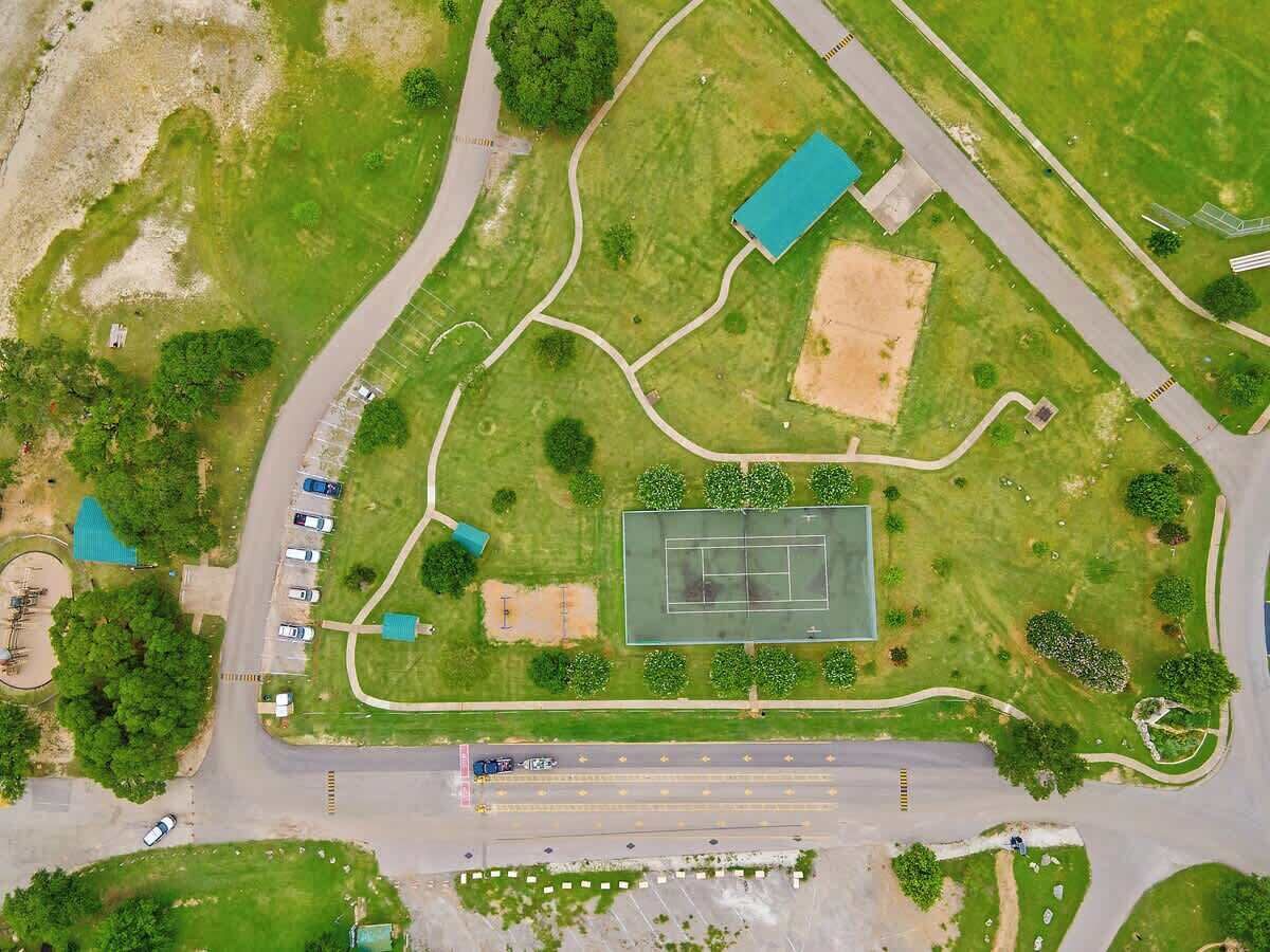 Vue aérienne d’un parc comprenant un court de tennis, des aires de stationnement et des espaces verts.