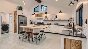 A modern kitchen with a central island, bar stools, a built-in oven, and a large window. - Family Relaxation: Private Pool & Spa with Games (Austin)