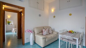 Un salon avec un canapé beige, une table à manger avec des chaises et un vase rempli de fleurs.