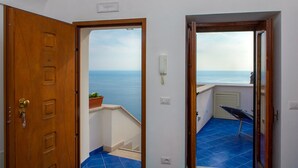 Un couloir avec une porte en bois et une vue sur la mer, visible à travers une porte ouverte.
