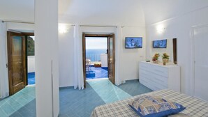 Une chambre avec un lit, une commode et un téléviseur. Elle dispose d’un balcon avec vue sur la mer.