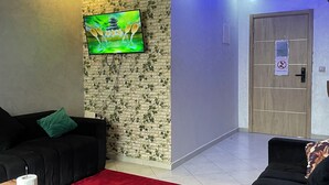 A modern living room with a black sofa, a red carpet, a wooden coffee table, and a TV mounted on a brick-patterned wall. - anza appartement (Agadir)