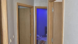 A hallway with wooden doors leading to a bedroom with a bed and a nightstand. - anza appartement (Agadir)