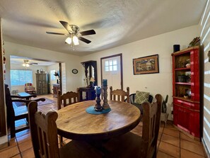 A dining area with a round wooden table, chairs, a ceiling fan, and a red cabinet with shelves.