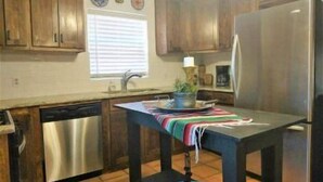 A kitchen with wooden cabinets, a stainless steel refrigerator, a dishwasher, and a window with blinds.
